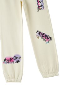 Beżowe dresy z nadrukowanymi grafikami: "NAJLEPSI", "PRZYJACIELE na zawsze" oraz "Super Miłość" w wyrazistym, wielokolorowym tekście. Elastyczne mankiety.