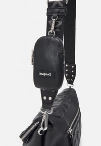 Sac bandoulière noir avec petite pochette détachable, fermetures éclair argentées et détails de la sangle et de la quincaillerie de marque.