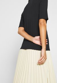 Top nero a maniche corte realizzato in tessuto liscio, abbinato a una gonna beige plissettata, che mette in risalto un silhouette semplice e moderna.