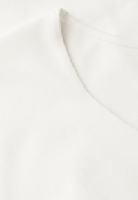 Tessuto di cotone bianco a scollo a V che mostra una consistenza liscia e una leggera lucentezza, con cuciture definite lungo il colletto e la cucitura della spalla.