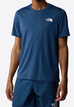 Tummansininen lyhytnukkainen urheilupaita, joka on valmistettu kosteutta siirtävästä kankaasta. Paidassa on valkoinen logo vasemmassa rinnassa ja pyöreä pääntie.