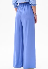 Lichtblauwe, wijde broek gemaakt van een gladde stof met een elastische tailleband, die een losse pasvorm en vloeiende uitstraling biedt.