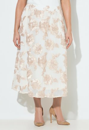 Weißer Midirock mit beiger Blumenstickerei, kombiniert mit passenden glitzernden beigen High-Heels an einer stehenden Person.