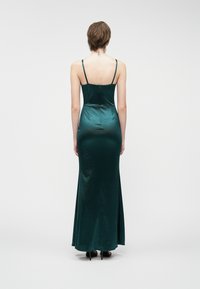 Μεγάλο βραδινό φόρεμα από σατέν σε σκούρο πράσινο, με λεπτές τιράντες, κομψή εφαρμογή και ευθεία τελείωση που φτάνει μέχρι τ�ο πάτωμα.
