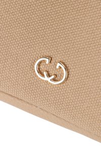 Beige kanvas tegnebog med en struktureret overflade, guldfarvet hardware-logo og en glat læderkant i bunden.