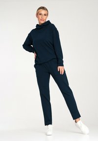 Granatowa bluza z kapturem o luźnym kroju, zestawiona z pasującymi spodniami cargo z bocznymi kieszeniami, noszona z białymi trampkami.