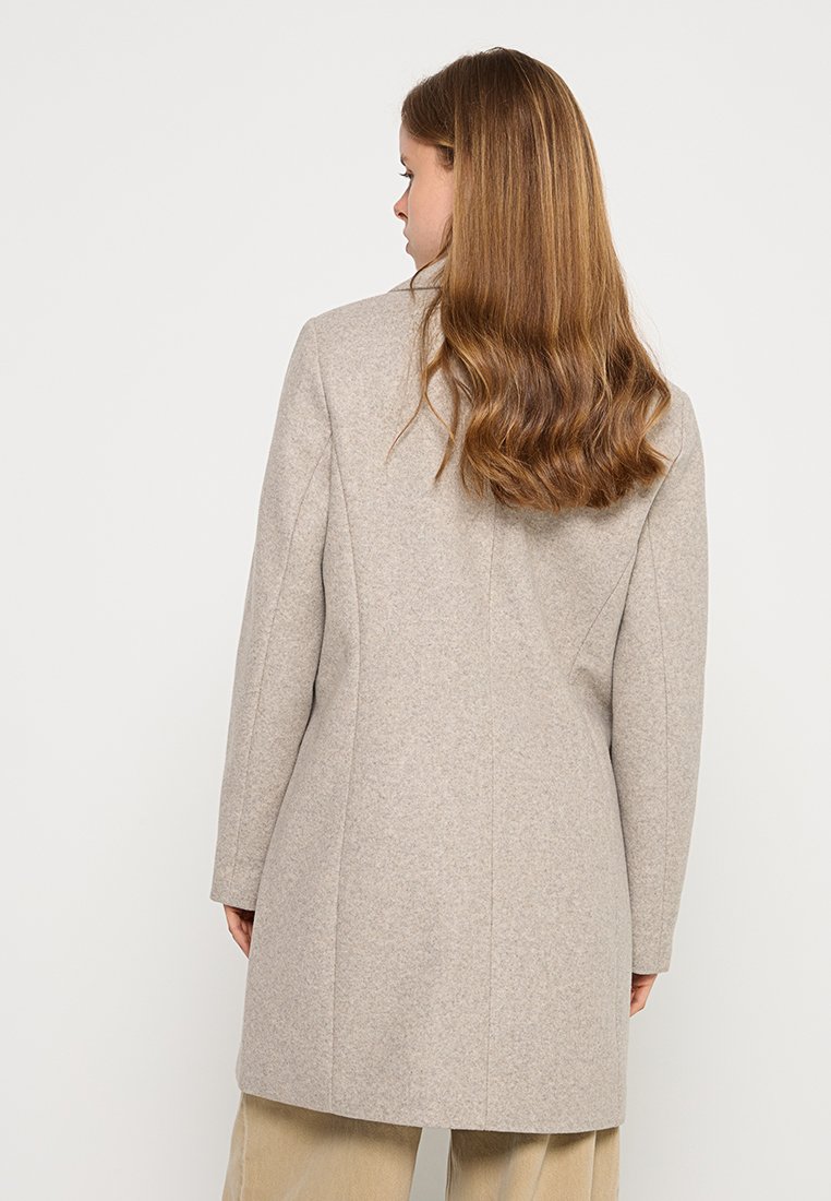 Abrigo largo beige con un corte entallado, fabricado en un suave tejido de mezcla de lana. Presenta una silueta recta y un diseño minimalista, sin cierres visibles.