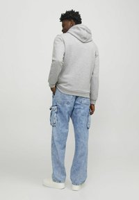 Sudadera gris con capucha, con un dobladillo acanalado. Combinada con jeans cargo azul claro con bolsillos laterales y zapatillas blancas.