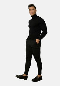 Un haut noir à manches longues et col roulé associé à un pantalon noir slim et des mocassins marron, avec un design texturé et des détails accentués.