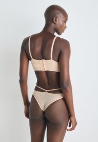 Naken ribbet bh og bikini-sett med justerbare stropper og krok-lukking. Bakdelen har minimalistisk design med tynne side-stropper.