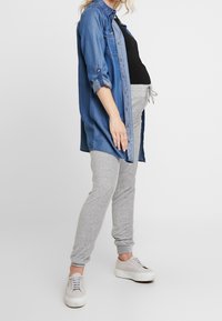 Jeansskjorta i blått, grå jerseybyxor och ljusa sneakers. Skjortan har uppvikta ärmar; byxorna har resårmidja.