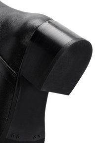 Bota de cuero negra con un tacón cuadrado y plano. Presenta una textura suave y un sutil pespunte alrededor del cuello. Sin marcas ni acentos visibles.