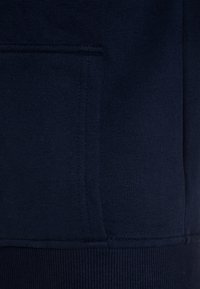 Marinblå sweatshirttyg med en slät textur, med en känguruficka och ribbade muddar. Minimalistisk design utan mönster.