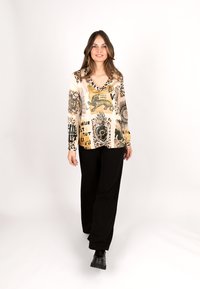 Long-sleeve, cream blouse featuring animal prints in black and gold, paired with black wide-leg trousers and black ankle boots.