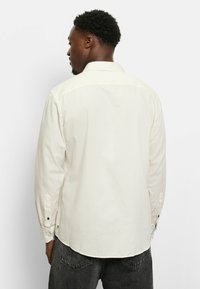 Langarmshirt aus leichtem Creme-Stoff, mit klassischem Kragen, geknöpftenÄrmeln mit marineblauen Akzenten und einem abgerundeten Saum. Flaches Rückendesign.