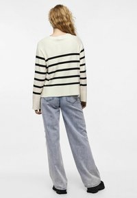 Kremgenser med svarte horisontale striper, løs passform, ribbede mansjetter, kombinert med lyseblå vide jeans og svarte platå-sko.