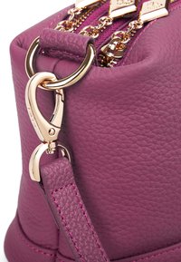 Lila Lederhandtasche mit strukturierter Oberfläche, ausgestattet mit goldfarbenen Metallbeschlägen und einem Clipverschluss. Mit passendem Schulterriemen.