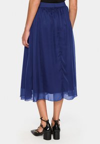 Gonna midi blu navy semi-trasparente con vita arricciata e tessuto morbido, abbinata a scarpe con tacco alto nere.