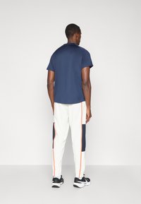 Ναυτικό πόλο μπλουζάκι σε συνδυασμό με λευκά joggers με ναυτικές και πορτοκαλί λεπτομέρειες. Τα joggers διαθέτουν σχεδίαση πάνελ και ελαστικούς μανσέτες.