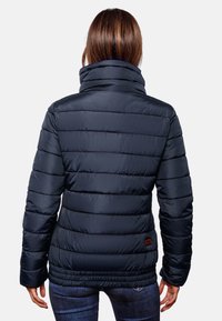 Marine pufferjack met een hoge kraag, geborduurd ontwerp en elastische onderkant. Heeft een logopatch op de linksonderkant. Glad, glanzend textuur.