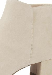 Botín de ante beige hasta el tobillo con tacón cuadrado. Presenta un diseño sin costuras, con costuras mínimas y una textura suave.