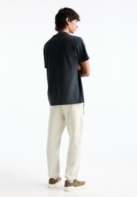 Dunkelgraues Baumwoll-T-Shirt mit kurzen Ärmeln, kombiniert mit hellbeigen Sweatpants. Schuhe in Olivgrün mit weißer Sohle.