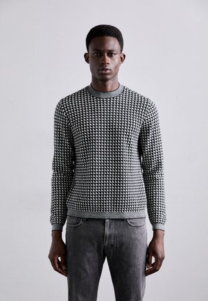 Maglione a fantasia bianca e nera con collo rotondo, maniche lunghe e un design texture. Abbinato a jeans di denim grigi.