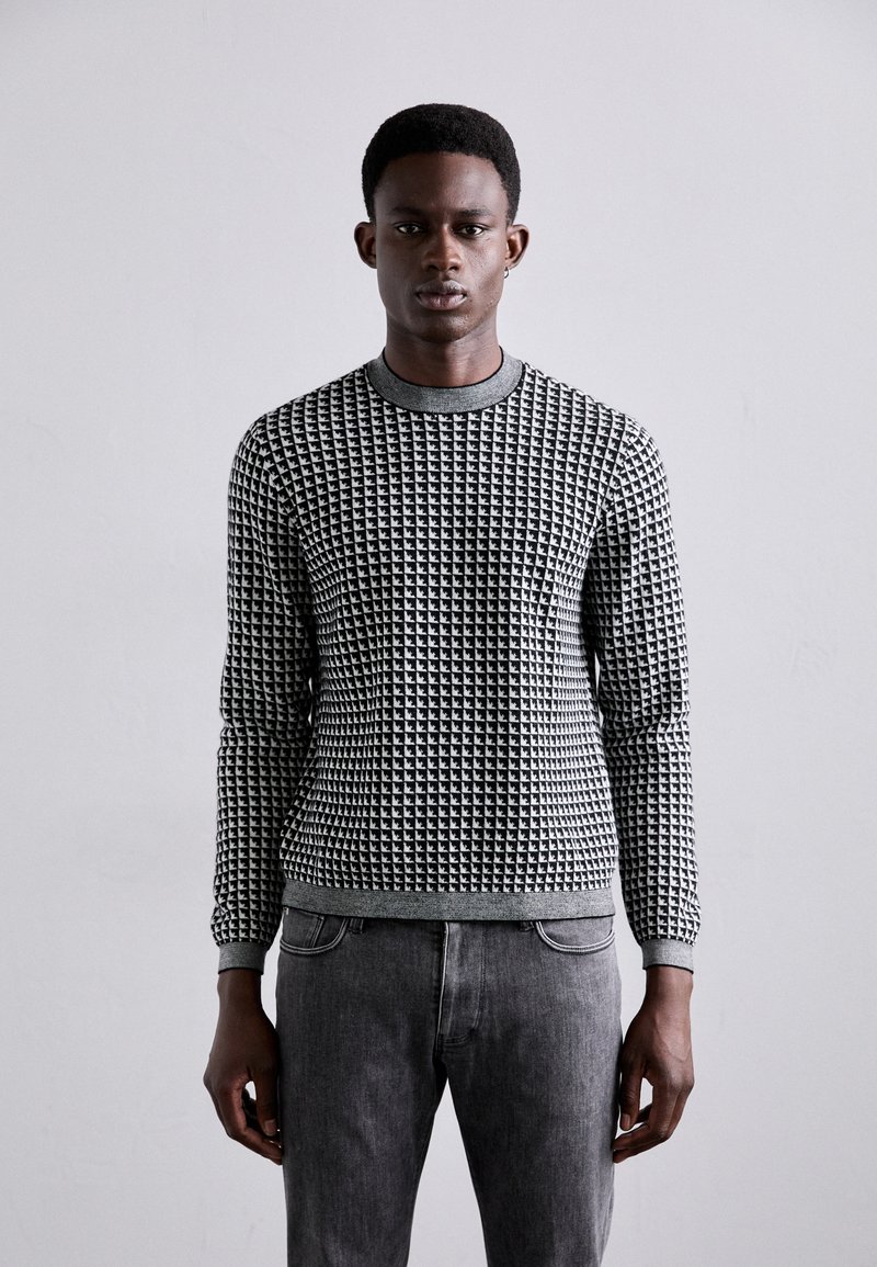 Pull en noir et blanc à motif avec col rond, manches longues et design texturé. Associé à un jean en denim gris.