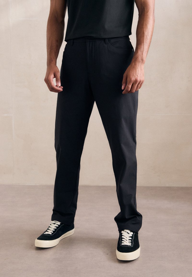 Pantaloni negri cu o croială dreaptă, având un front plat, buzunare laterale, dintr-un material uşor, asortaţi cu tenişi din suede verde.
