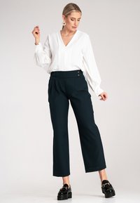 Biała bluzka z dekoltem w serek i bufiastymi rękawami, zestawiona z ciemnozielonymi spodniami z wysokim stanem i akcentami w postaci guzików. Całość dopełniają czarne buty na platformie.