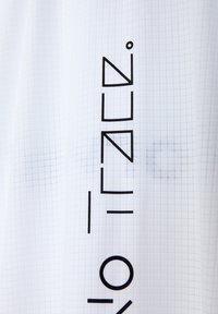 Weißer strukturierter Stoff mit einem Rastermuster und kräftigen schwarzen geometrischen Buchstaben, die senkrecht angeordnet sind. Sauberes, modernes Design.