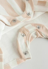 Nahaufnahme von beige-weiß gestreifter Babybekleidung mit Metall-Druckknöpfen auf weichem Stoff.