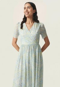 Lyseblå omlægningskjole med korte puffærmer, prydet med et blomstermotiv i gult og grønt. Skørten er samlet ved livet.