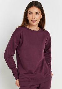 Sudadera burdeos de tela suave con cuello redondo, mangas largas y puños acanalados. Presenta un corte relajado y sin patrones visibles.