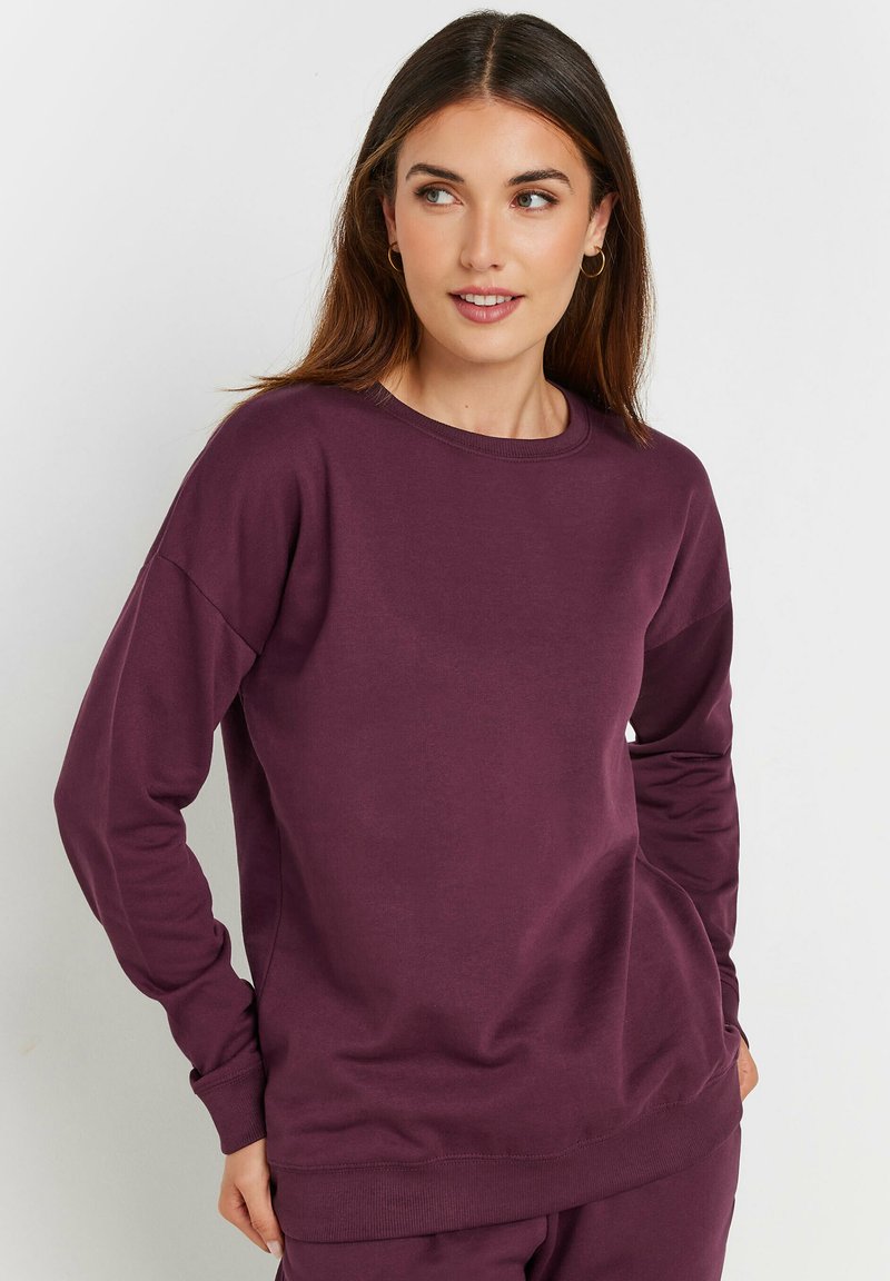 Sudadera burdeos de tela suave con cuello redondo, mangas largas y puños acanalados. Presenta un corte relajado y sin patrones visibles.