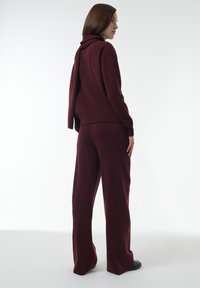 Bordeaux gebreide trui met een col en een gedrapeerde achterkant, gecombineerd met bijpassende wijde broekspijpen, beide met een gladde, zachte textuur.