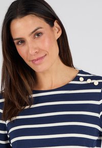 Top a righe navy e bianche con scollatura rotonda e tre bottoni decorativi bianchi sulla spalla sinistra. Tessuto morbido.