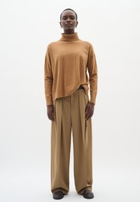 Brun rullekrave sweater med afslappet pasform, kombineret med beige plisserede bukser. Glat stoffet med et minimalistisk design.