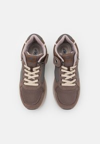 Sapatilhas de malha castanhas com detalhes cinzentos, atacadores em creme, colarinho acolchoado e destaque do logotipo proeminente. Bico arredondado e sola de borracha.