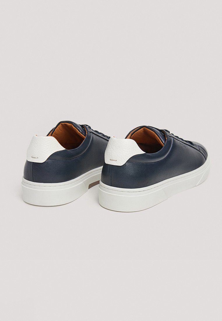 Baskets en cuir bleu marine avec un capuchon de talon texturé blanc, semelle en caoutchouc blanche et intérieur marron. Bout arrondi et design minimaliste.