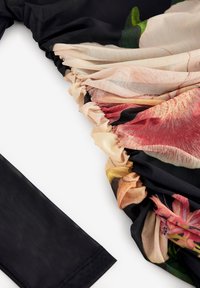 Tissu floral transparent avec bords froncés fixé à un tissu en maille noire solide, montrant une texture détaillée et des coutures sur fond blanc.