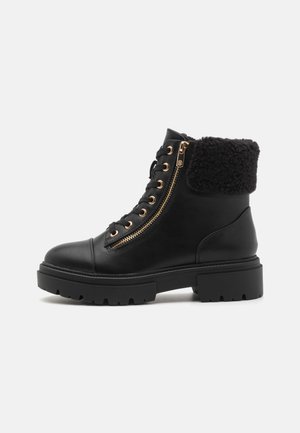 Bottines en cuir noir avec un bout arrondi, des accents dorés, des doubles zips et un revers en fausse fourrure noire. Semelle en caoutchouc épaisse avec traction.