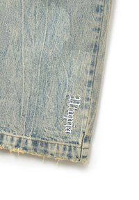Los jeans de mezclilla azul claro cuentan con un dobladillo deshilachado y un logotipo bordado de "Mango" en blanco cerca de la parte inferior. La tela tiene una textura sutil.