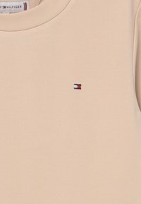 Beżowy bawełnowy t-shirt z okrągłym dekoltem i małym haftowanym logo w niebieskie, białe i czerwone akcenty na lewej piersi.