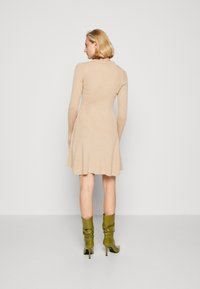 Kleid mit langen Ärmeln in Beige und schwingendem Rock, ausgestattet mit einer feinen gerippten Textur. Kombiniert mit grünen, lässigen High-Heel-Stiefeln.