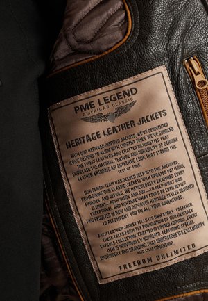 Čierna kožená bunda s hnedou visačkou, na ktorej je zlatým písmom vyrazený text. Visačka popisuje starostlivosť, dizajnovú filozofiu a jedinečnosť každej bundy.