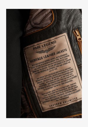 Czarna skórzana kurtka z brązowym metkiem z wytłoczonym tekstem. Metka opisuje pielęgnację, filozofię designu oraz indywidualność każdej kurtki.