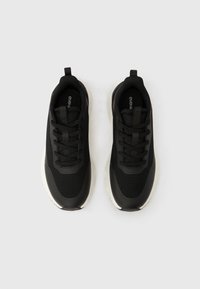 Ζευγάρι μαύρα αθλητικά παπούτσια με κορδόνια και λευκές σόλες, φωτογραφημένα από πάνω σε απλό φωτεινό φόντο.