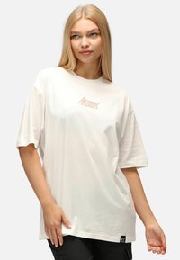 Weißes T-Shirt mit kurzen Ärmeln, das ein hellrosa "Action Comics"-Logo zeigt. Lockere Passform mit Rundhalsausschnitt und weicher Baumwolltextur.