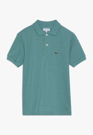 Camiseta polo de manga corta en color verde azulado con dos botones y logo de cocodrilo de Lacoste en el pecho, colocada plana sobre un fondo blanco.